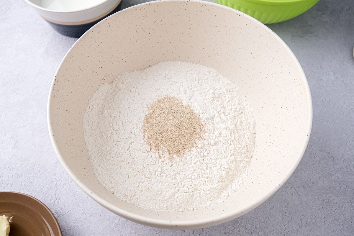 white mixing bowl filled with flour and yeast sitting on counter top.