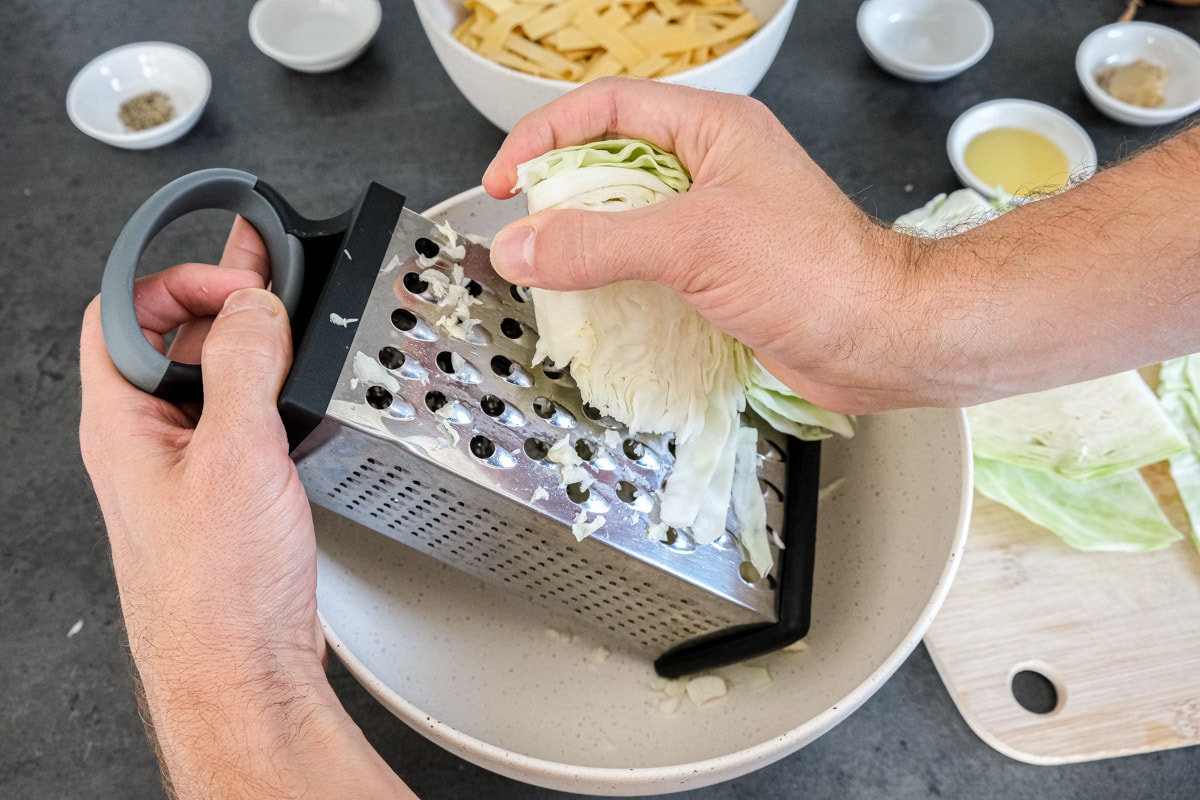 hand shredding wedge of cabbage on silver box grater.