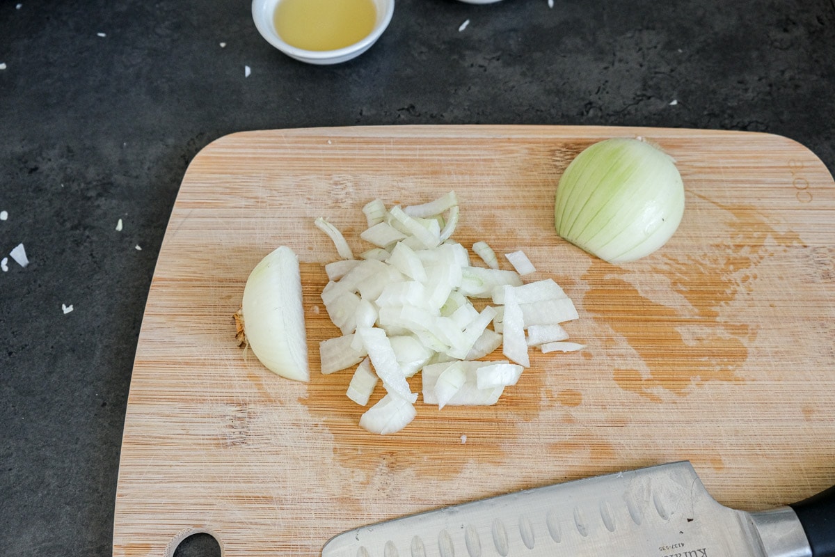 half an onion diced on wooden cutting board on counter.