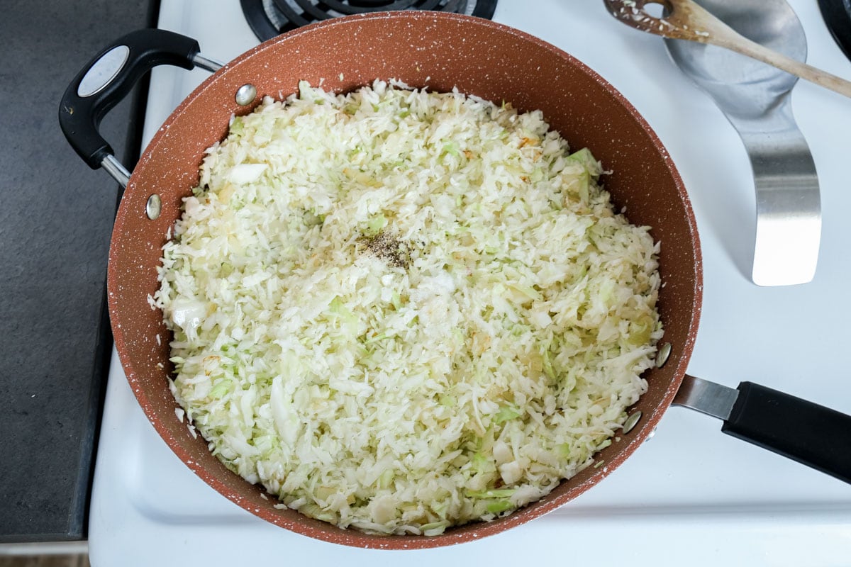 shredded cabbage in frying pan with spices on top not mixed in.