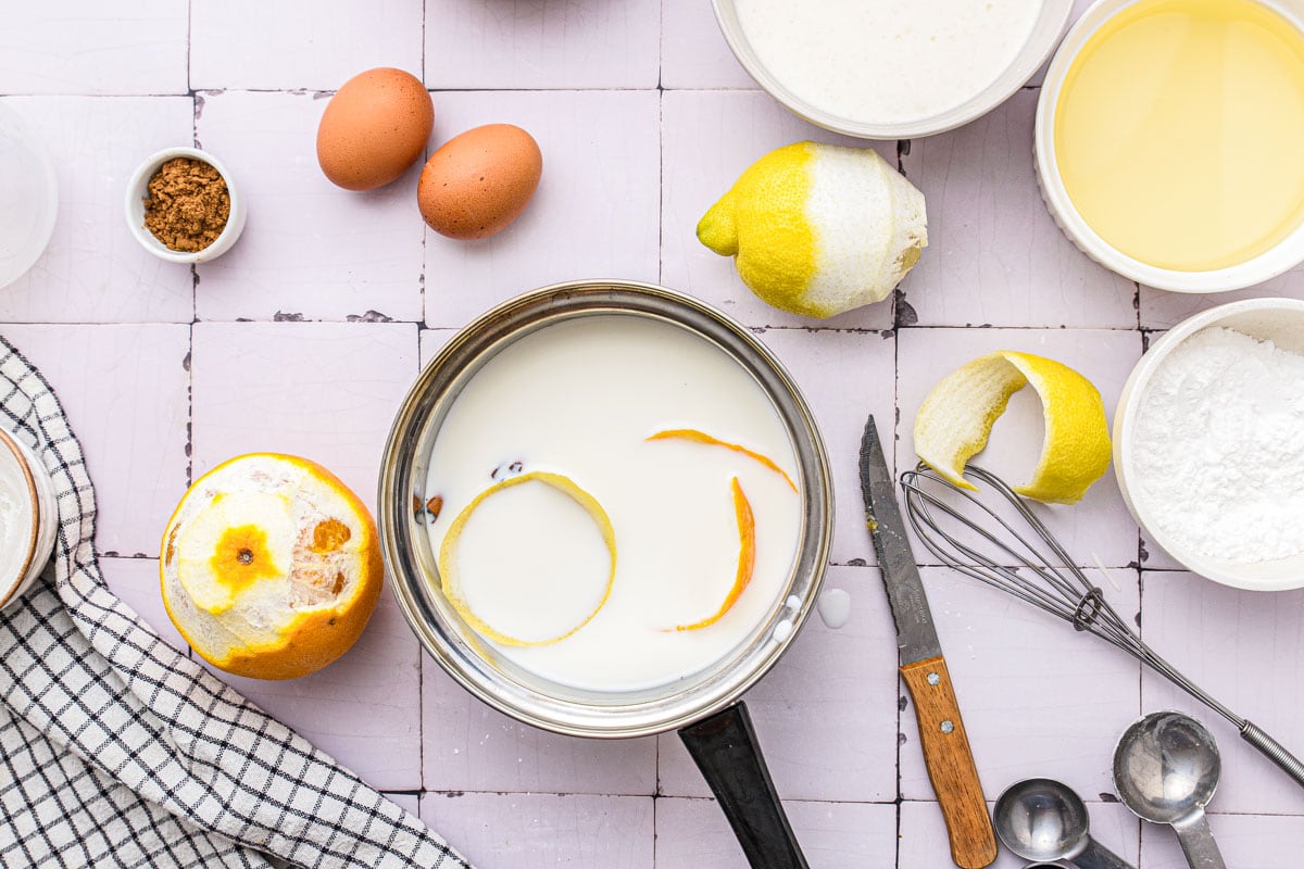 orange and lemon peels floating in milk in silver pot on counter top.