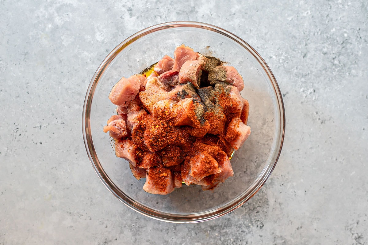 raw pork pieces covered in spices in clear glass bowl.