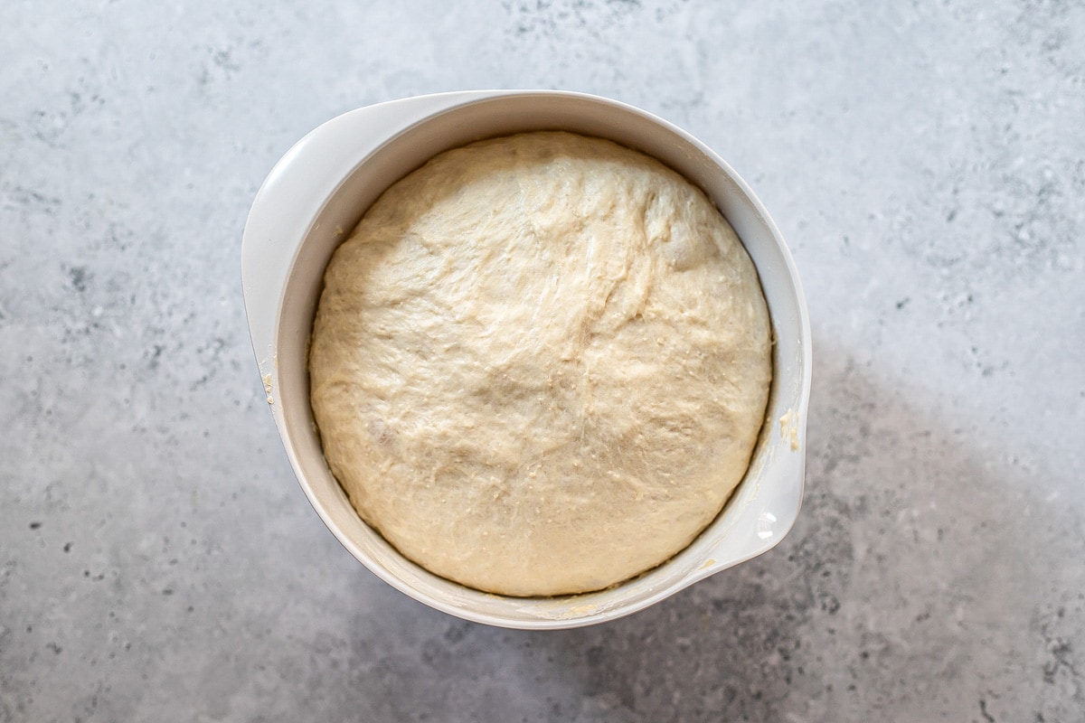 ball of risen pizza dough in mixing bowl on counter.