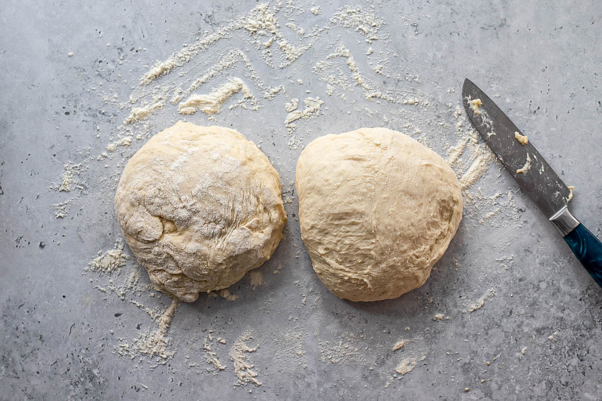 two balls of dough of equal size on counter top with knife beside.