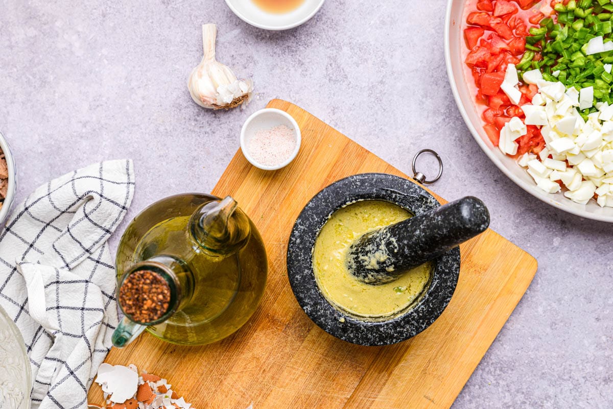 black mortar and pestle with crushed yellow dressing inside on wooden cutting board.