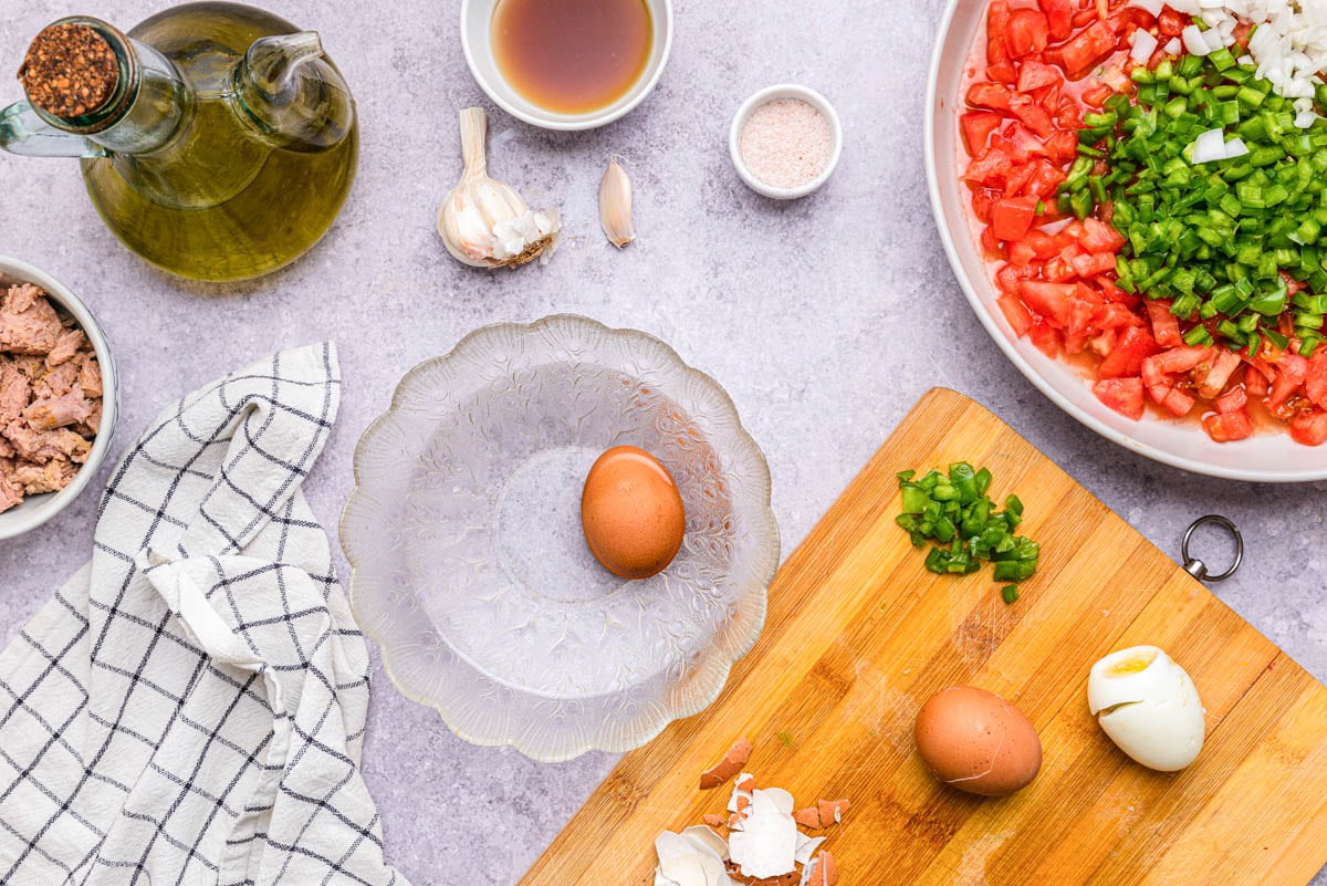 egg in clear bowl on counter with wooden cutting board beside with other eggs on it.