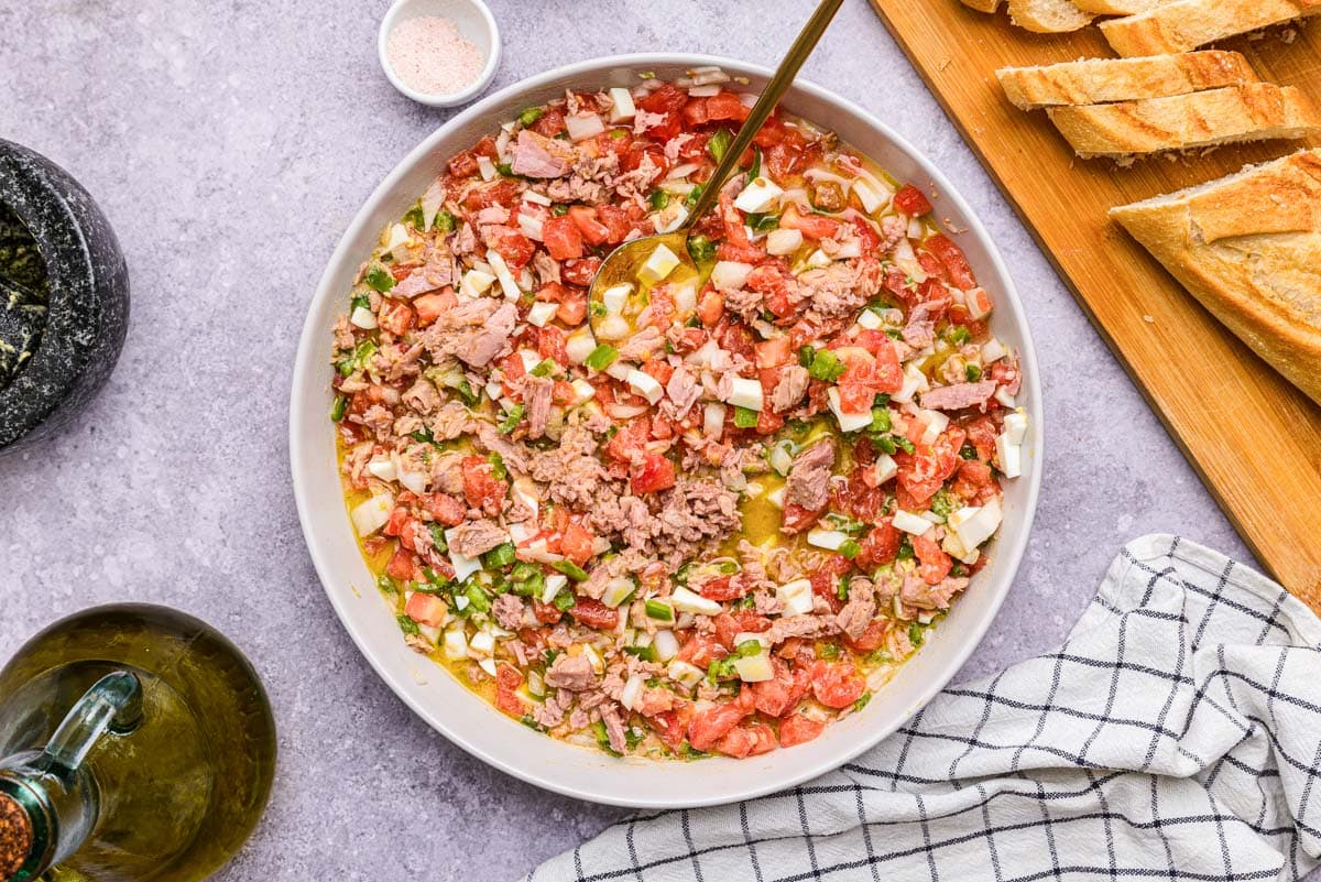bowl of spanish salad on counter with cutting board beside.