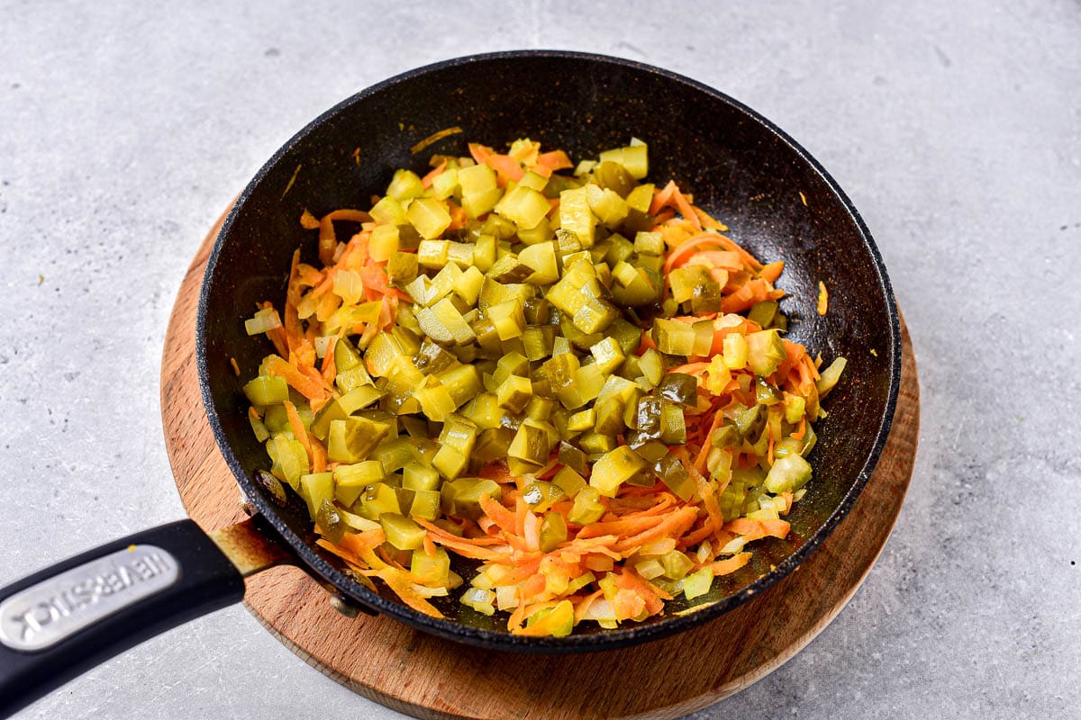 chopped pickles on top of shredded carrots in frying pan on round wooden board.