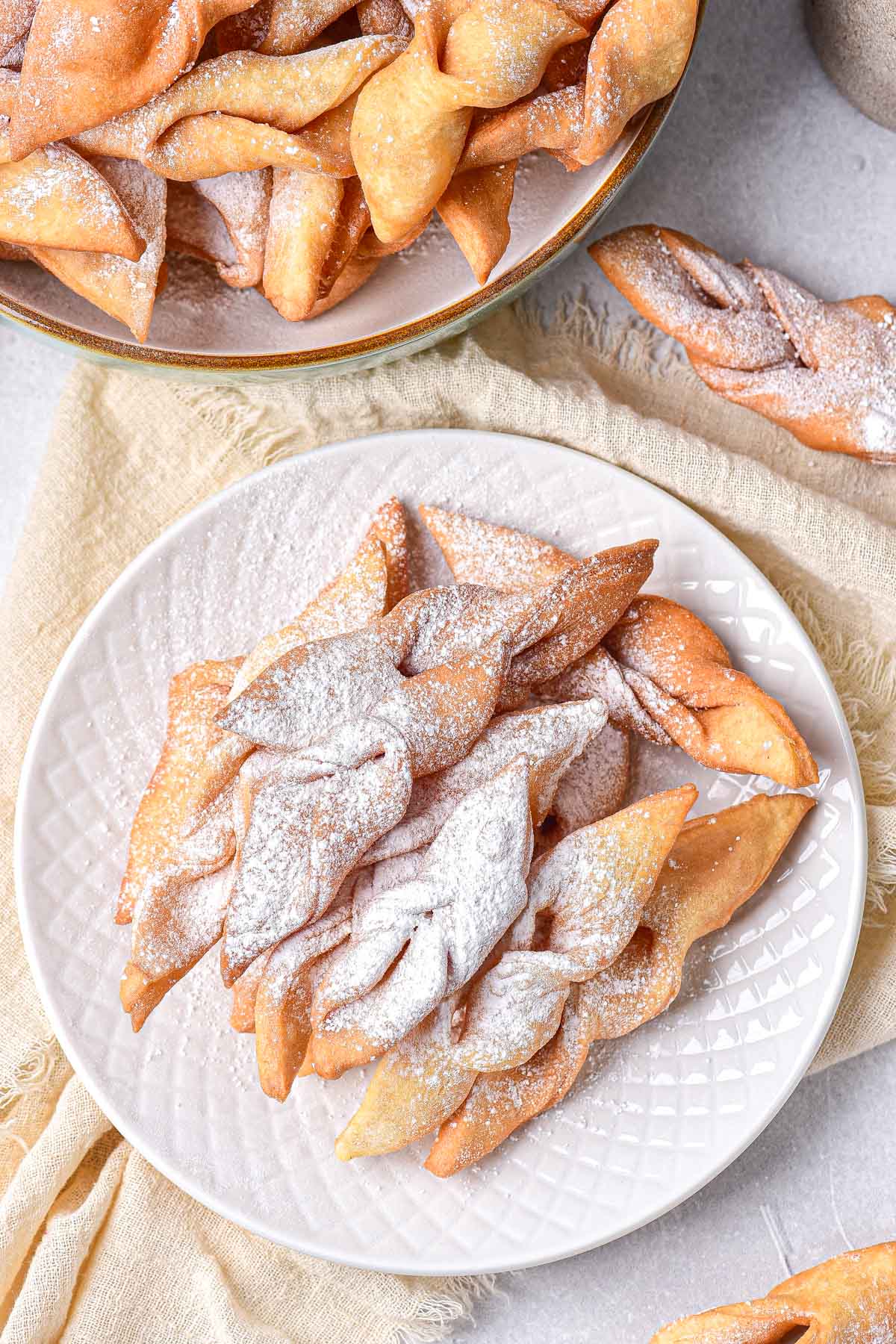 round white plate covered in fried cookies covered in powdered sugar.