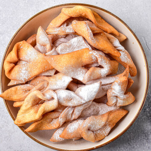 round plate of fried cookies covered in powdered sugar.