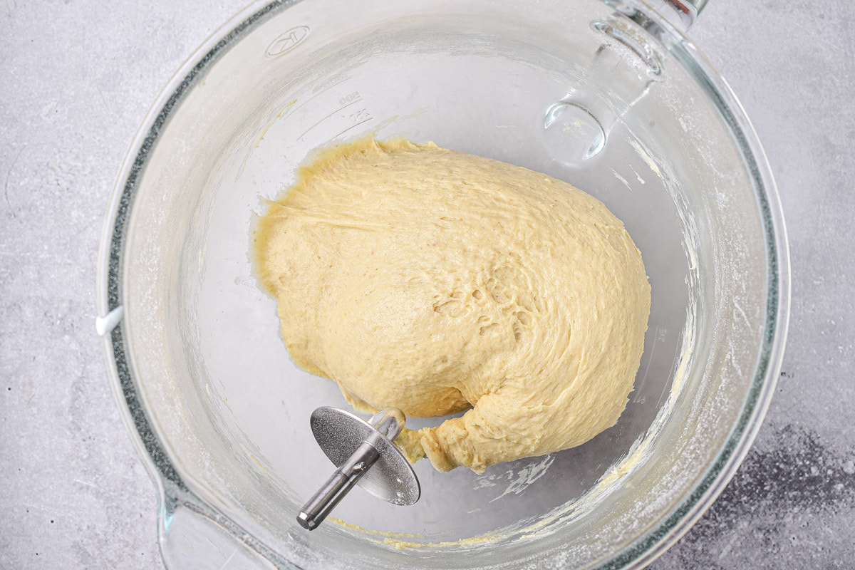large ball of dough in clear glass mixing bowl with metal mixing device still inserted.