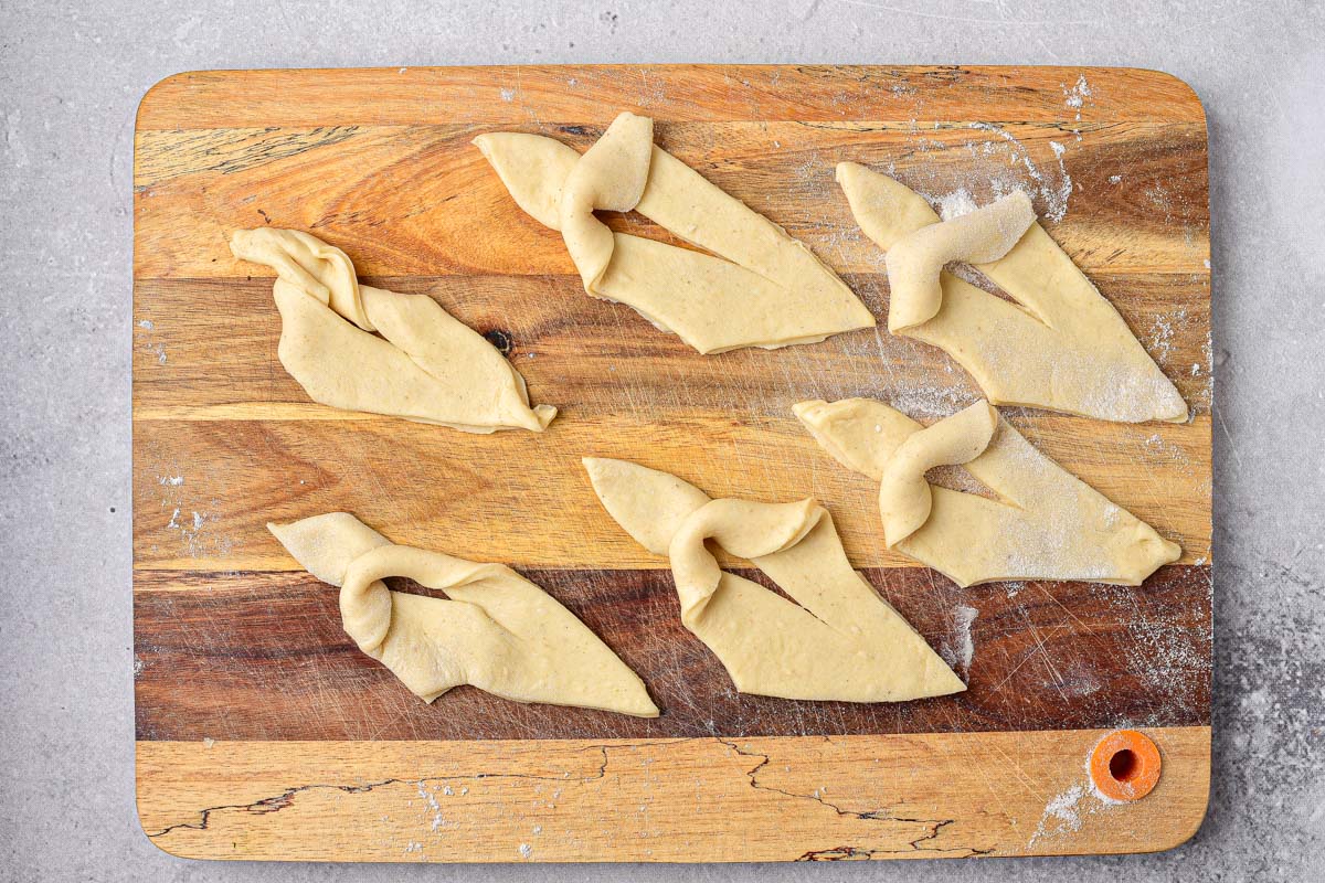 flat raw dough pieces cut and folded into themselves resting on wooden board.