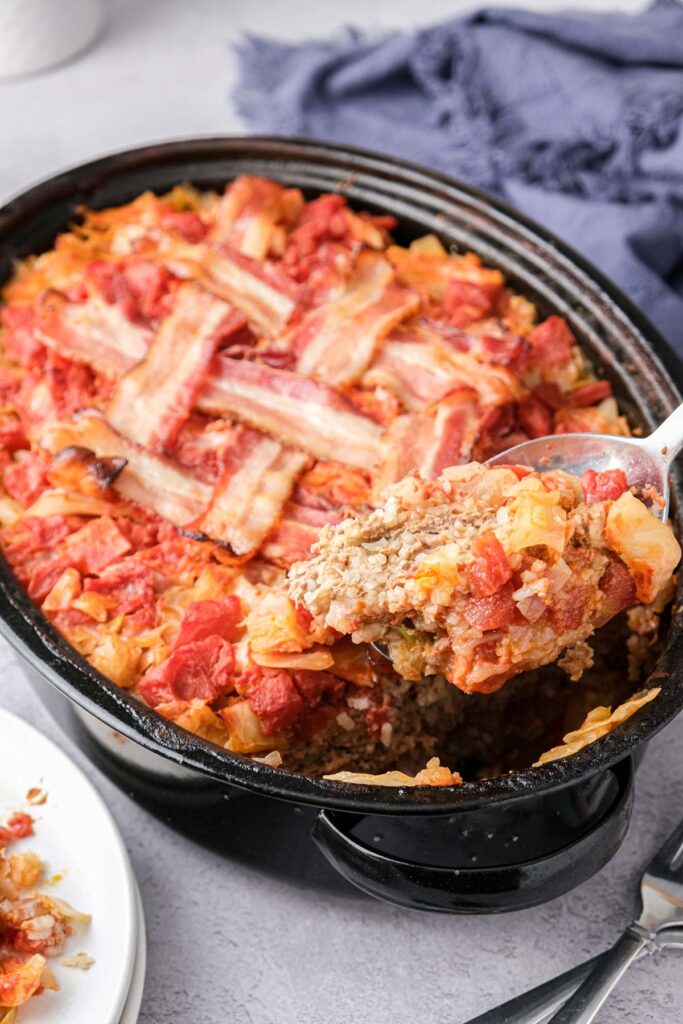 black roasting pan of cabbage roll casserole with spoon removing some in front.