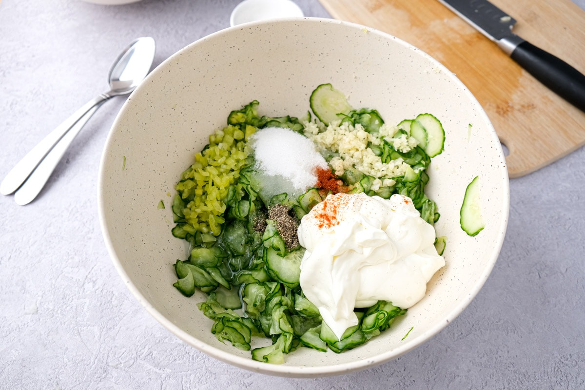 ingredients to make cucumber salad in white mixing bowl on counter.