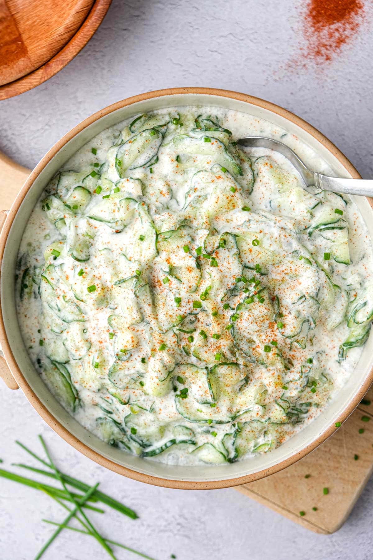 large serving bowl of cucumber salad seen from above with chives and paprika on top.