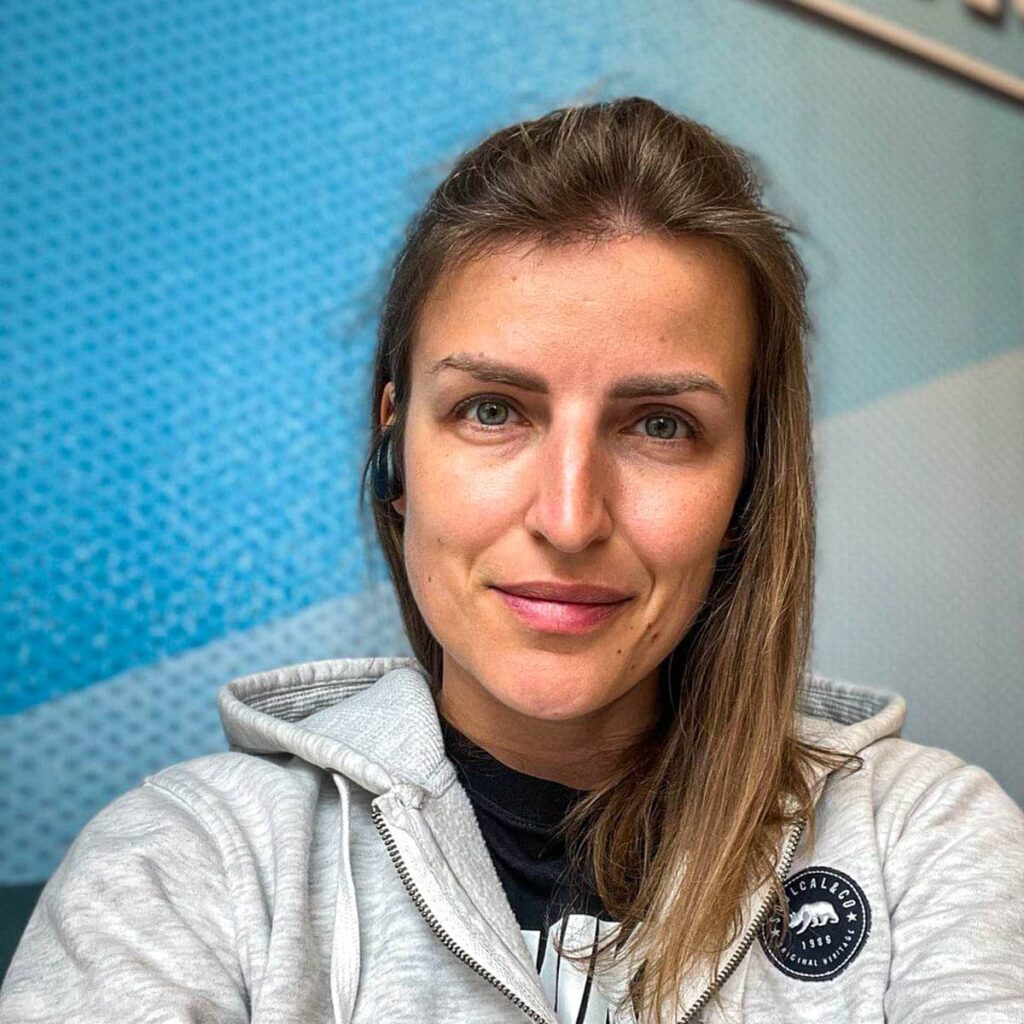 smiling woman wearing sweater with blue wall behind.
