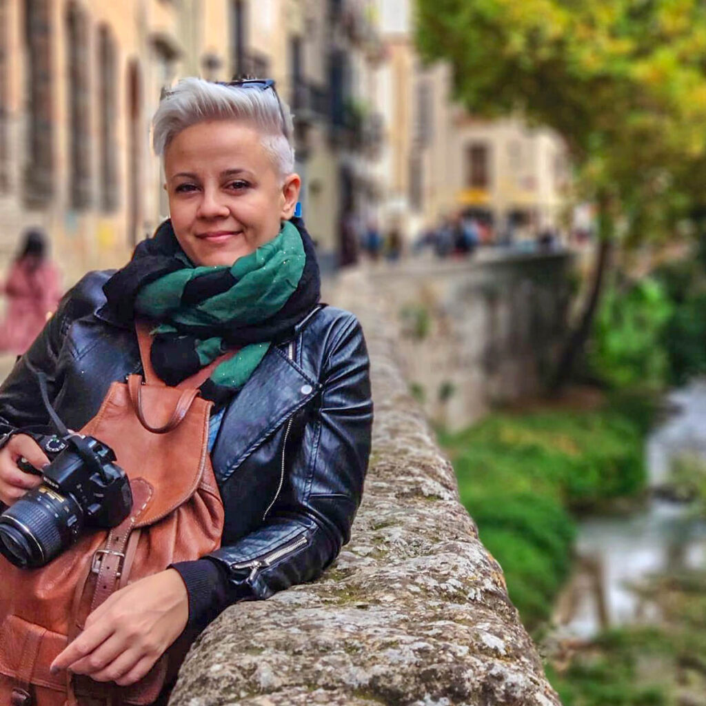 woman with black jacket leaning against old stone wall.