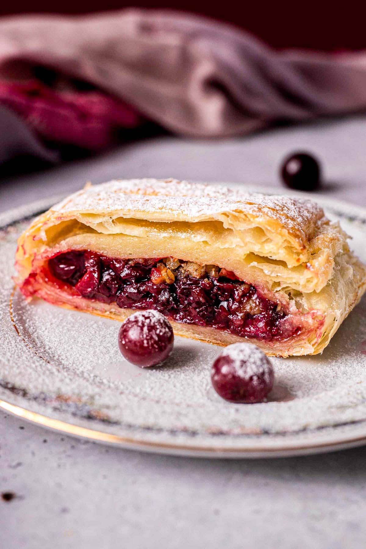 slice of cherry strudel on plate with whole cherries around.