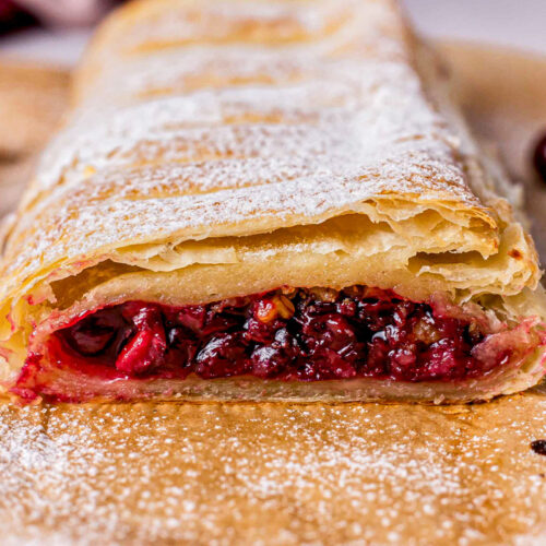cherry strudel laying on parchment paper with end cut off showing filling.