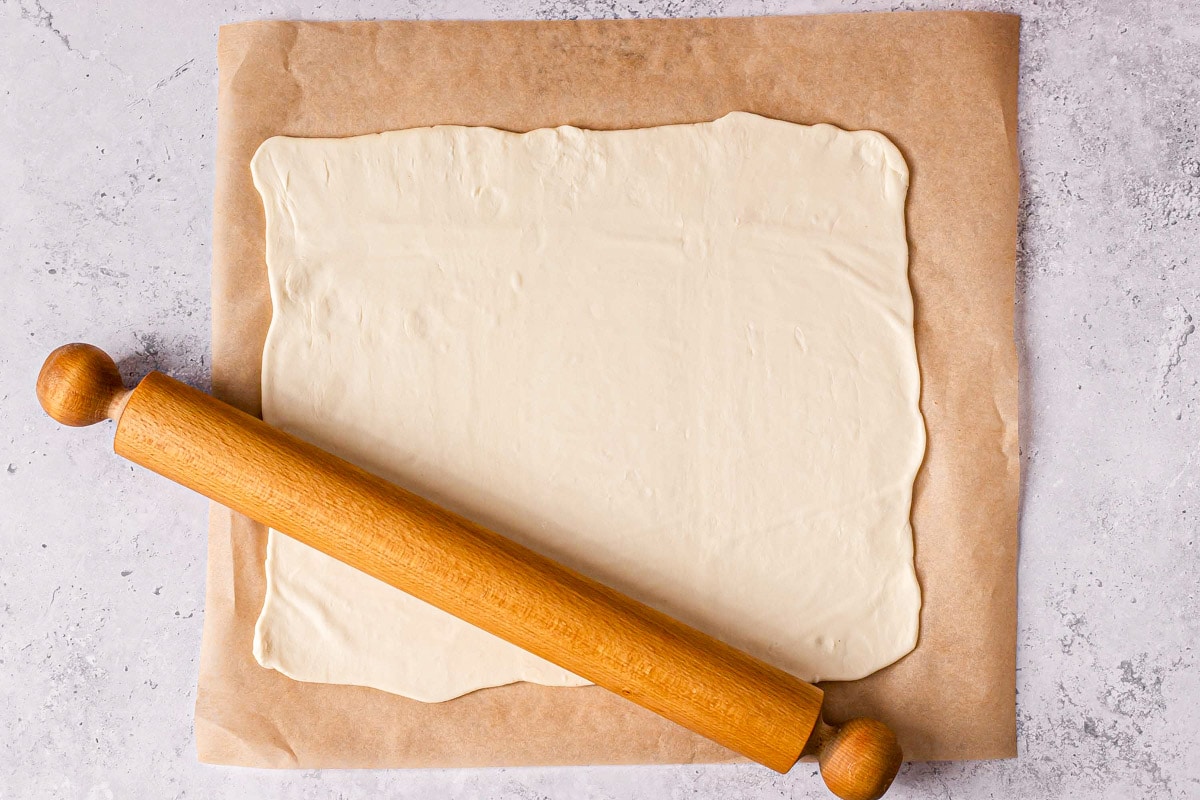 wooden rolling pin laying on top of flattened dough square on parchment paper.