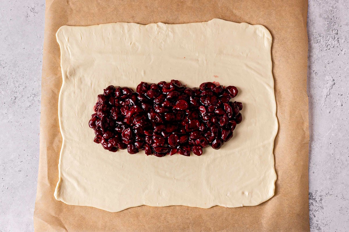 open square of dough on parchment paper filled with cherry filling in the middle.