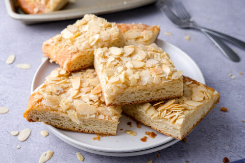 slices of butter cake covered in sliced almonds sitting on white plates.