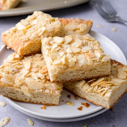 slices of butter cake covered in sliced almonds sitting on white plates.