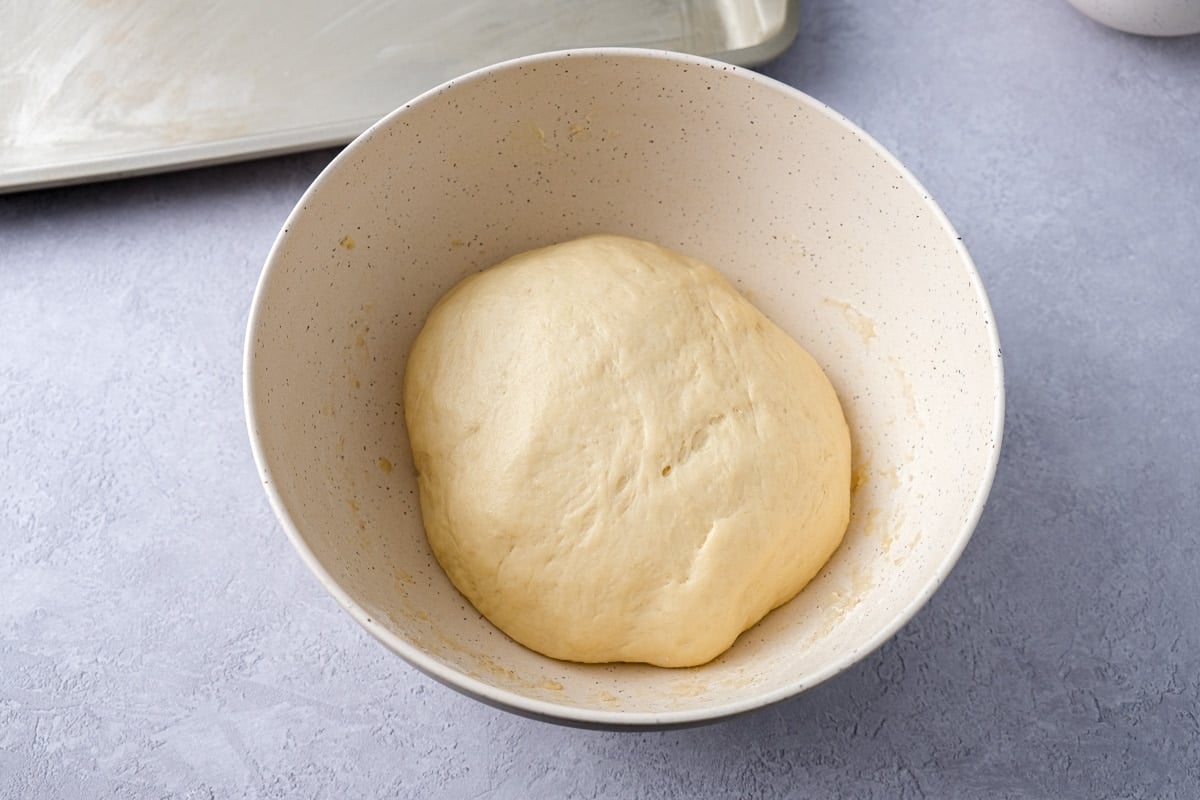 risen ball of dough in white mixing bowl on counter.