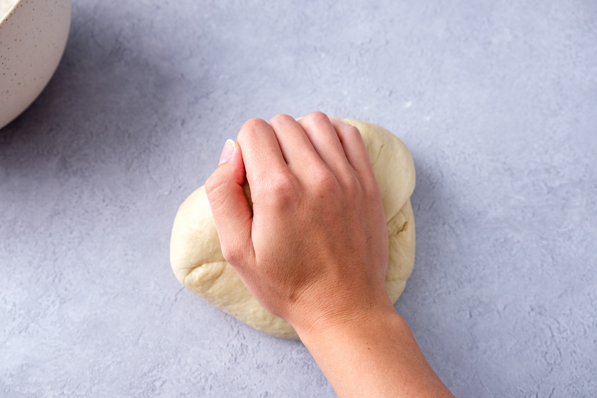 hand kneading ball of dough in counter top.