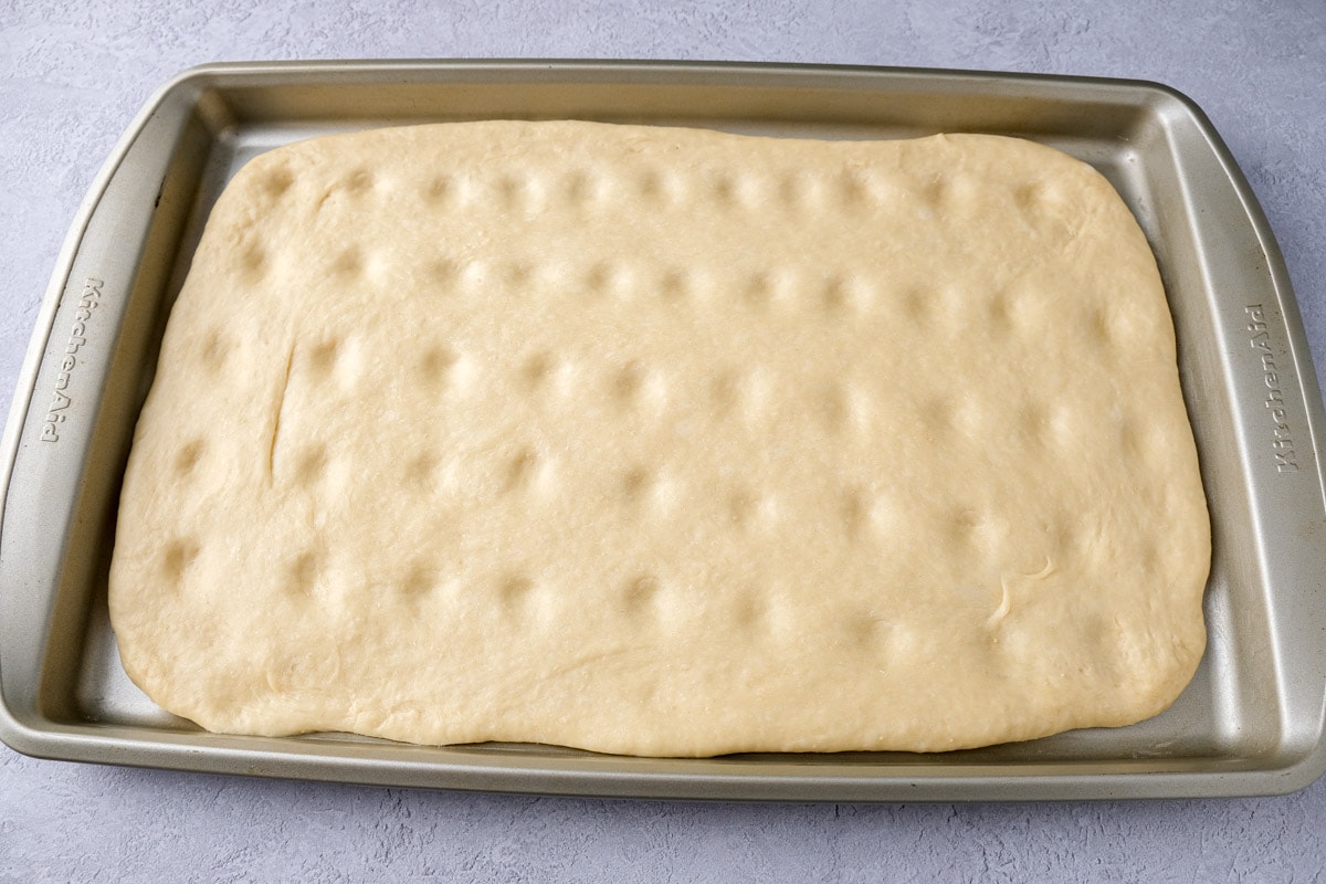 baking sheet covered in dough with small dents in the top sitting on counter.
