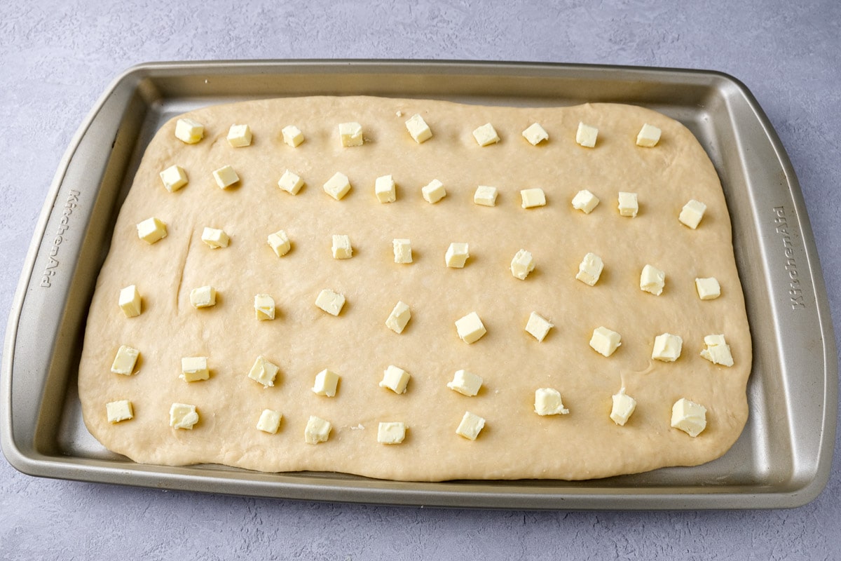chunks of butter arranged in rows on raw dough sitting in baking pan.