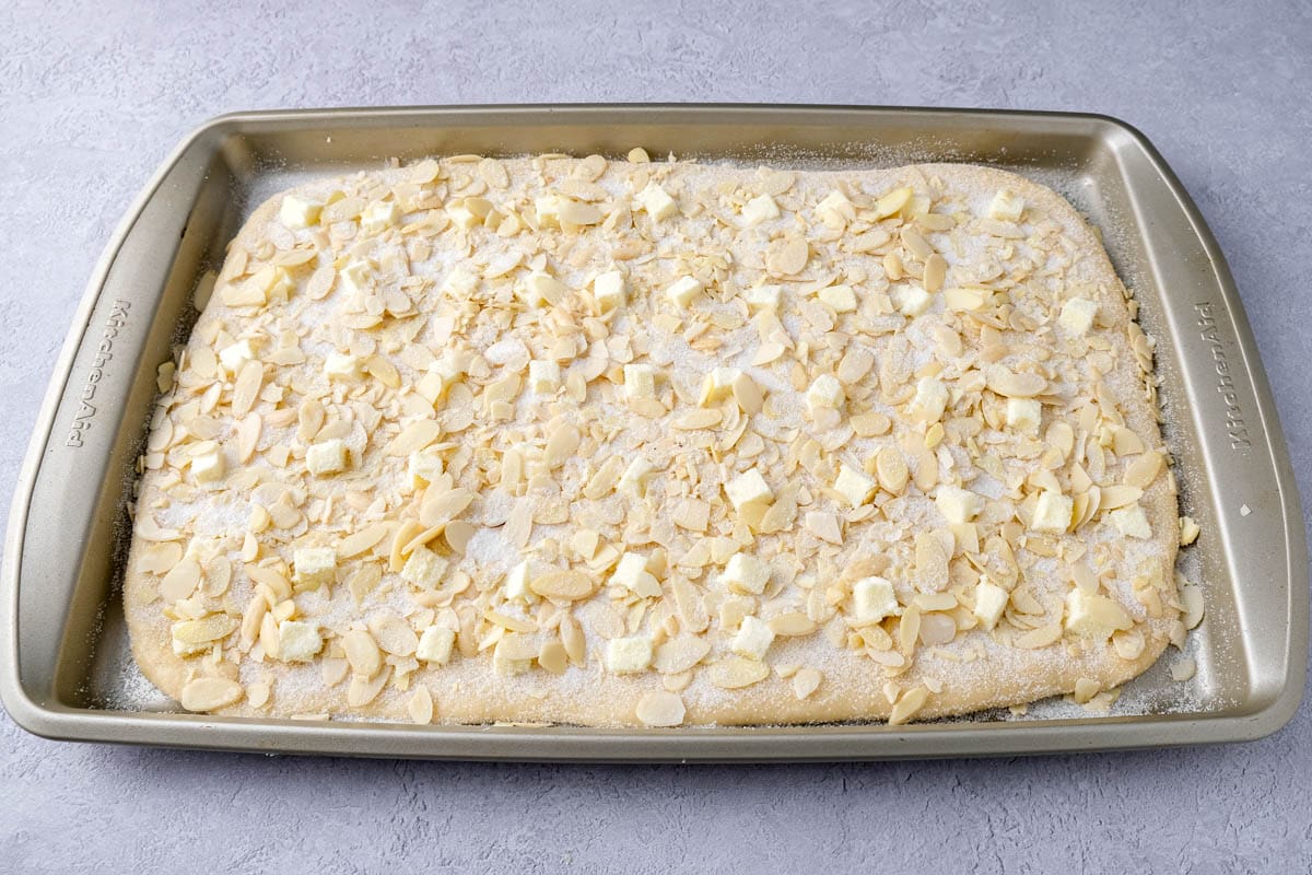 raw butter cake in rectangle baking sheet with almonds and sugar on top.