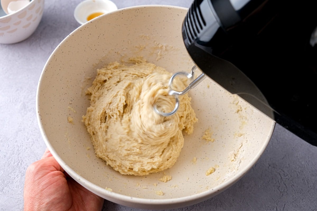black electric mixer kneading dough in white mixing bowl.