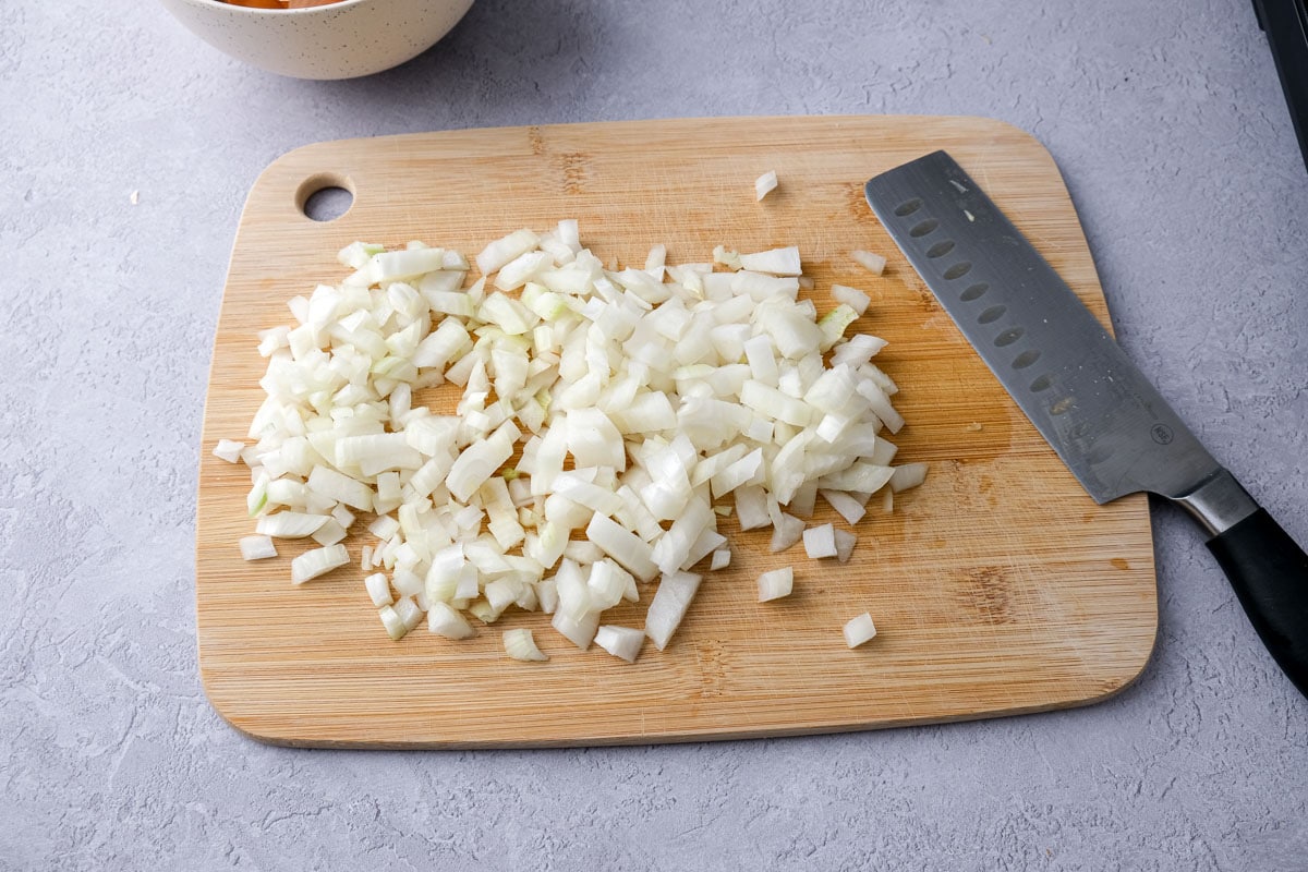 chopped onions on wooden cutting board with knife beside.