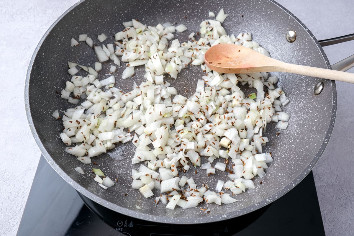 chopped onions with caraway seeds and wooden spoon stirring in frying pan.