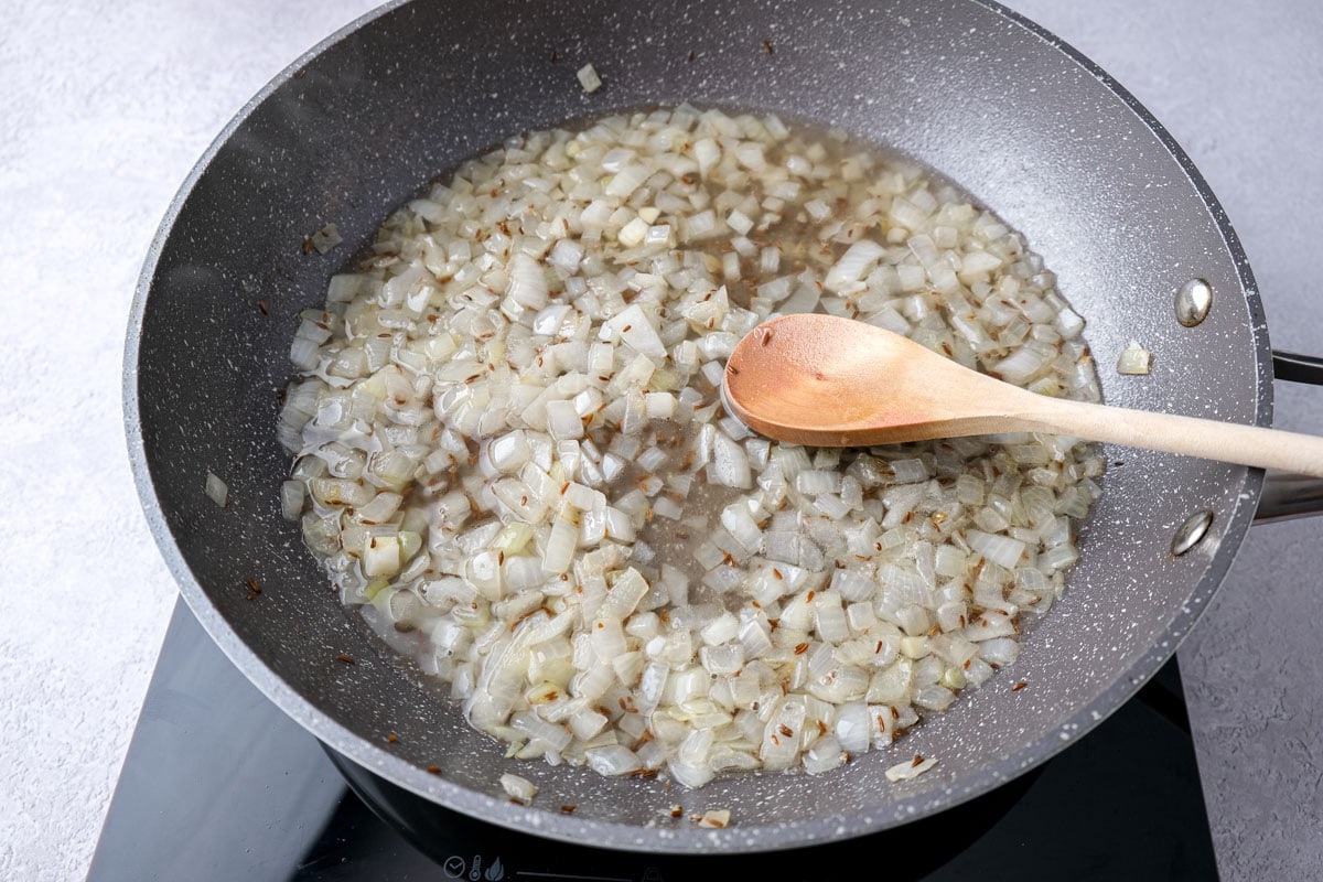onions and vinegar and water in frying pan with wooden spoon sticking out.