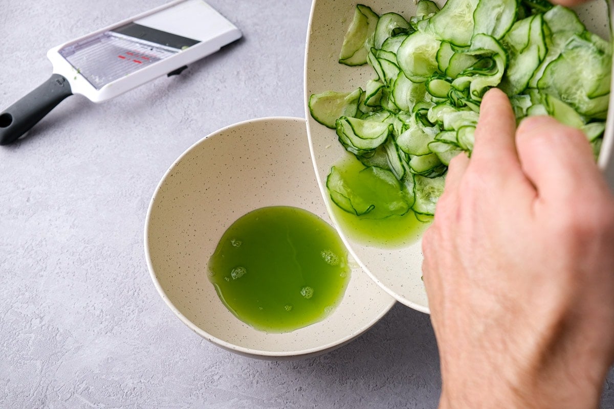 hand holding bowl of cucumber slices with smaller bowl of green juice below.