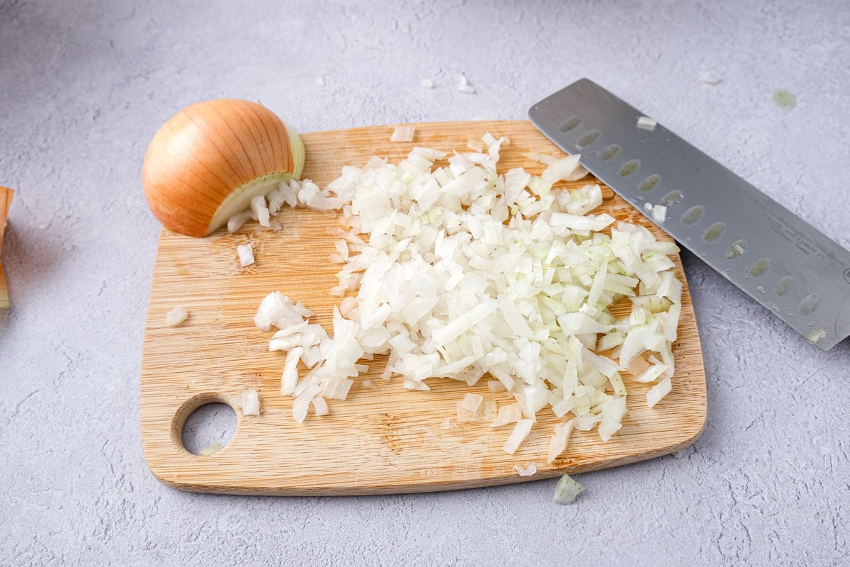 chopped yellow onion on wooden cutting board with knife beside.