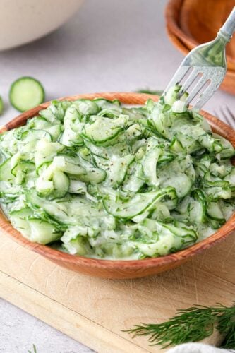 german cucumber salad recipe gurkensalat brown bowl with green cucumber salad and silver fork taking some away.