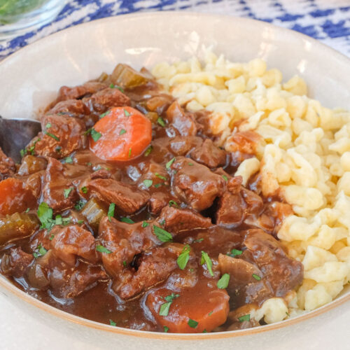 bowl of german beef goulash with spaetzle and fork beside on white counter top.