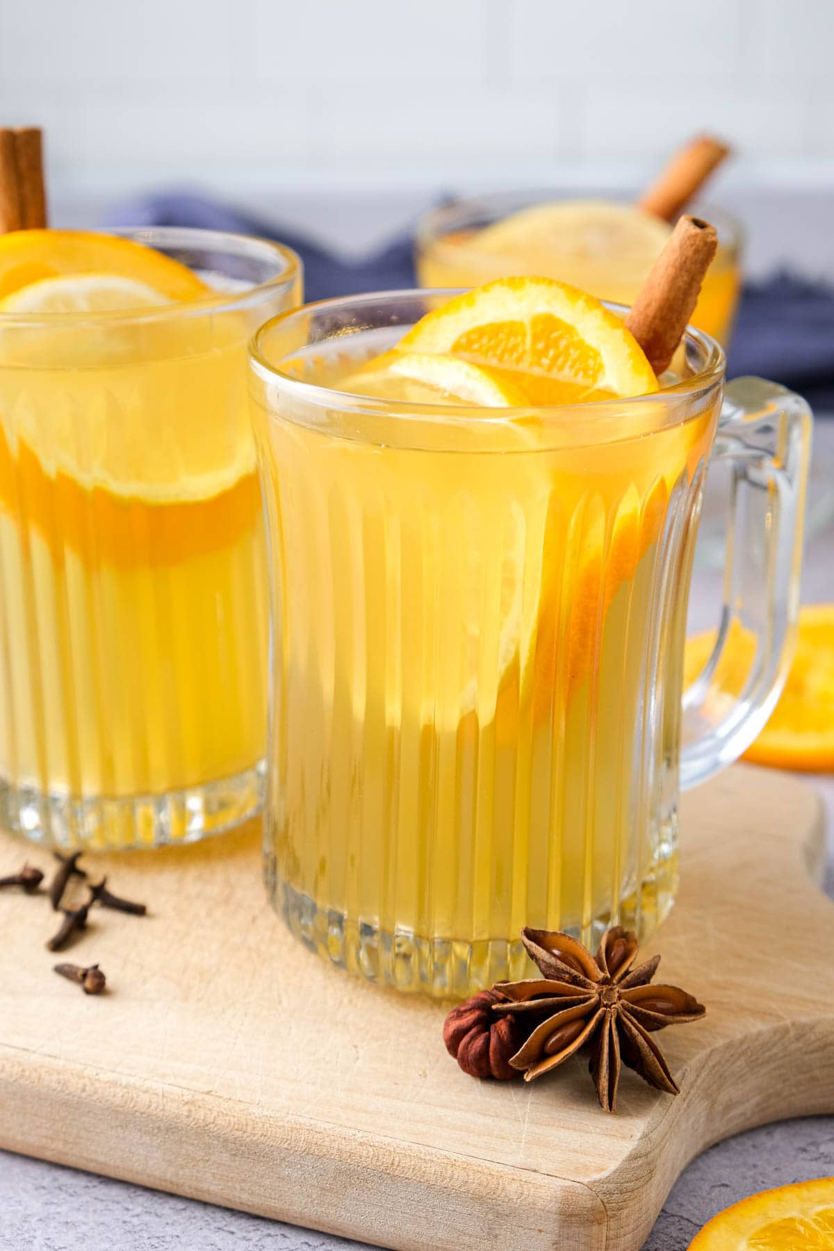 mugs of mulled white wine on wooden board with cinnamon sticks and citrus sticking out.