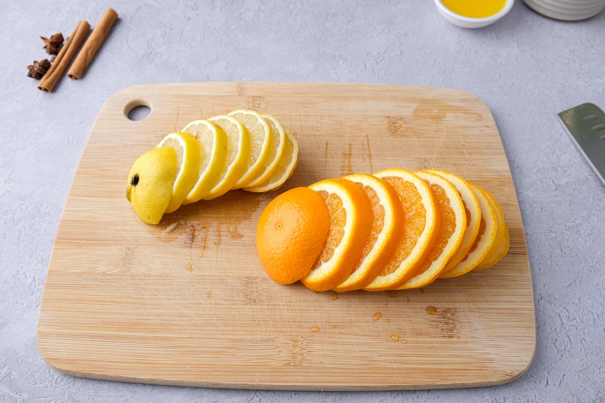 orange and lemon cut into slices on wooden cutting board on counter with spices around.