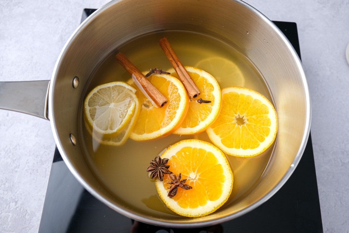 spices and sliced citrus in large silver pot on black hot plate.