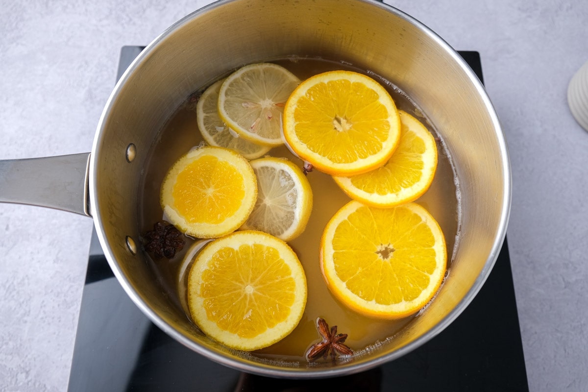 citrus slices floating in mulled white wine in pot on hot plate.