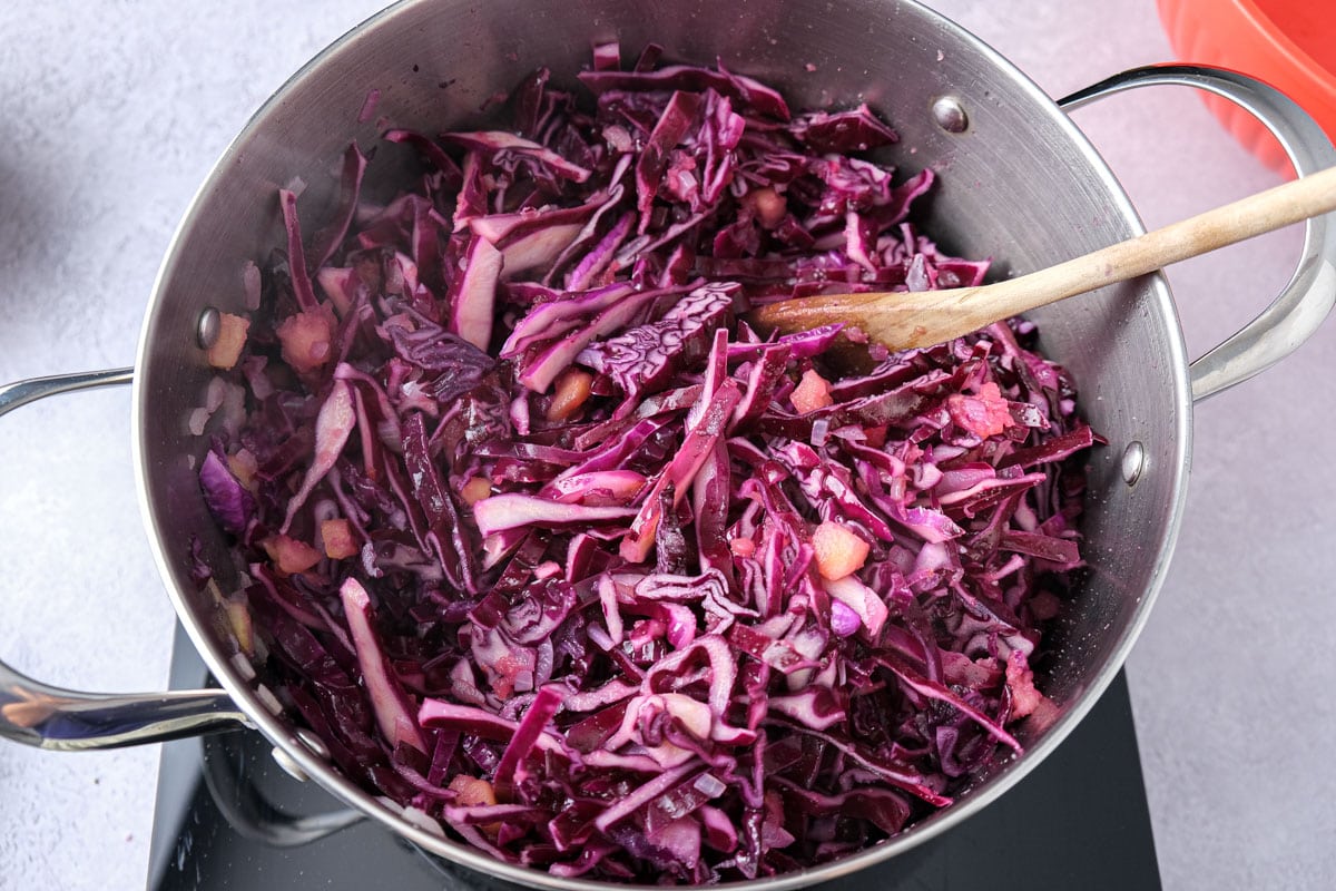 cooking red cabbage and apples in large silver pot with wooden spoon sticking out.