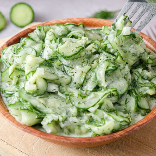 brown bowl with creamy cucumber salad with fork in it.