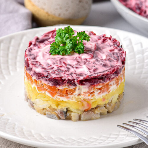 layered herring salad on white plate with two forks beside.