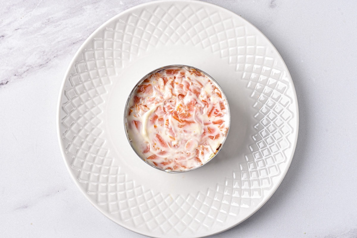 shredded carrots with layer of mayo on top in round metal form on plate.