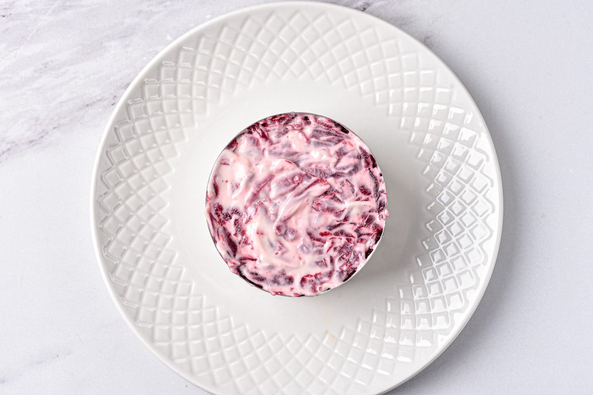 purple beets with mayo layer in round metal form on white plate.