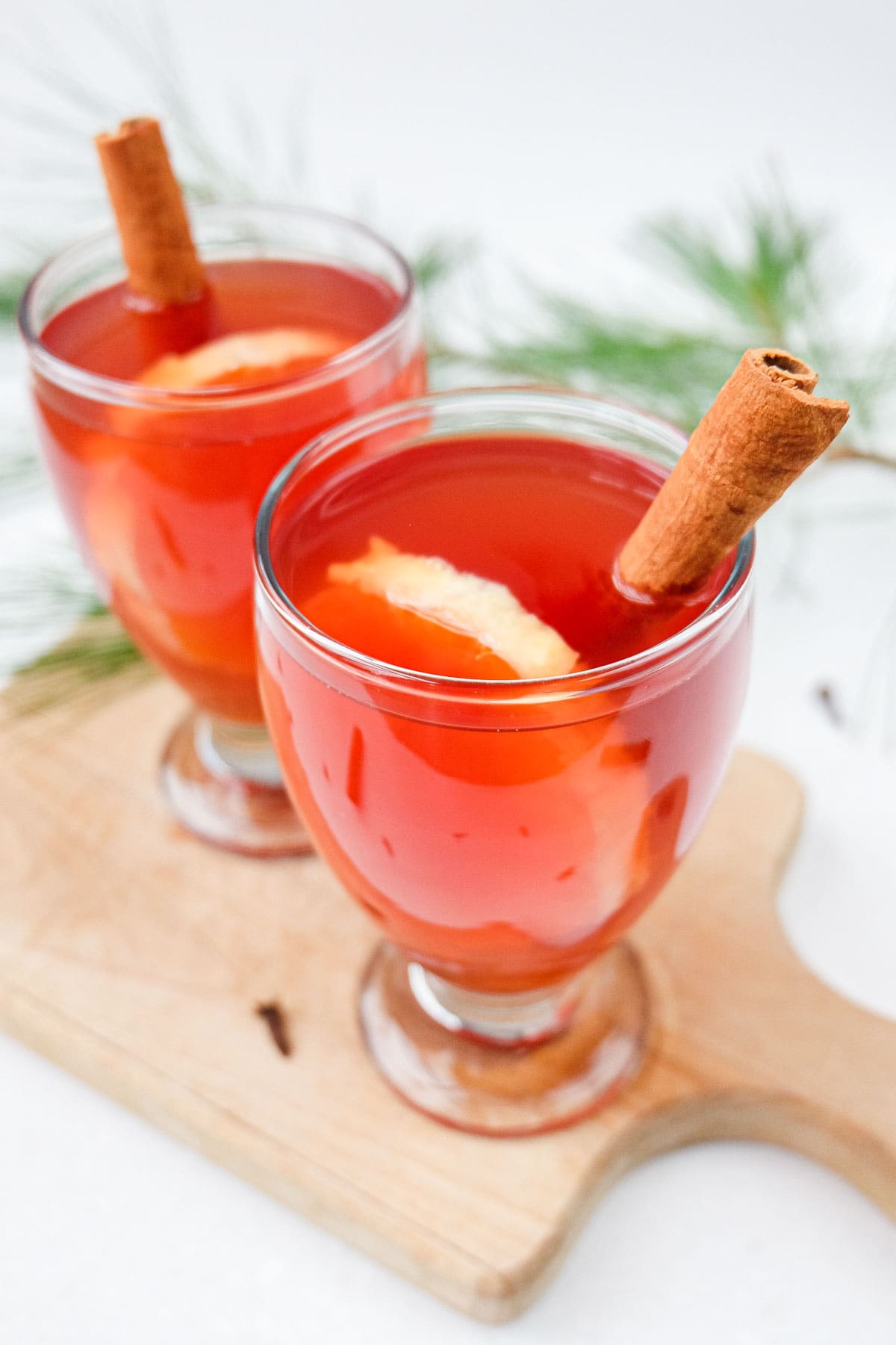 two glasses of red kinderpunsch on wooden board with cinnamon sticks.